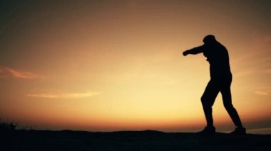 Adam şafak vakti deniz kenarındaki bir kayanın üzerinde gölge boksu yapıyor. Yavaş çekim videosu.
