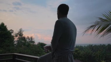 Gün batımının arka planında gözlüklü bir adamın silueti.