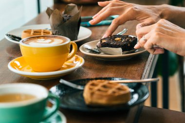 Bir kadının ellerini bir fincan kahve ve ahşap bir masada kruvasan tutarken yaklaş. 