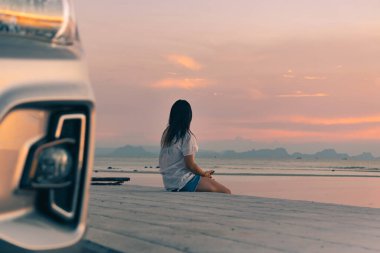 Genç bir kadın sette oturur ve deniz kenarında günbatımının tadını çıkarır.