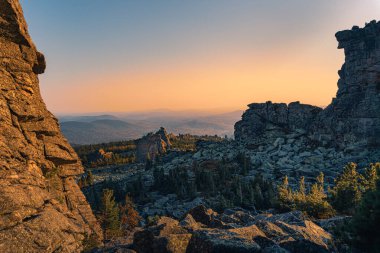 Bir dağın tepesindeki kayalık bir vadinin manzarası. Gün batımında mavi gökyüzüne karşı sıradağlar
