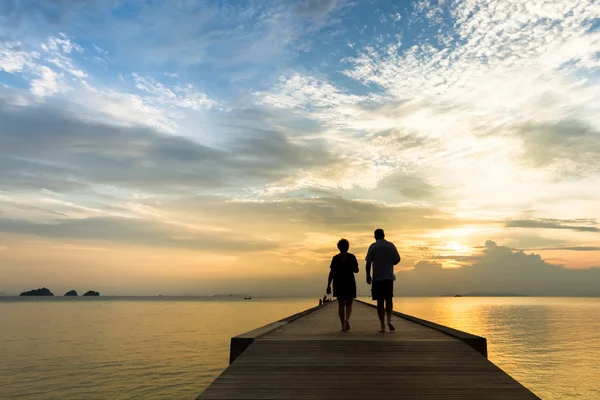 Elderly couple walking on the pier at sunset on a tropical island — Stock Photo, Image
