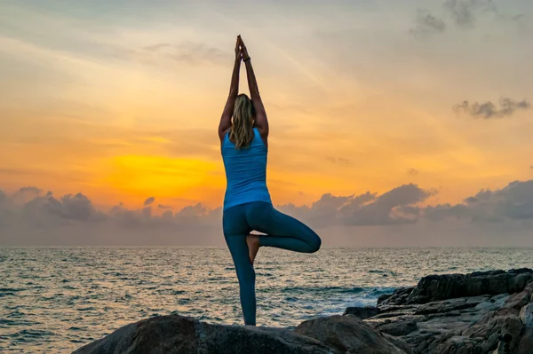 Молода жінка практикує йогу на каменях біля моря на світанку на тропічному острові — стокове фото