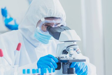 Erkek bilim adamı bilim laboratuarındaki mikroskop araştırmalarına bakar. Asyalı bilim adamı laboratuvar kimya laboratuvarlarını arıyor. Covid-19 Coronavirus biyokimya araştırma deneyi aşı konsepti