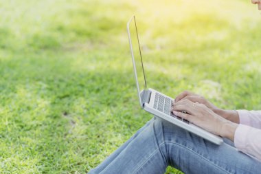 Asyalı kadın yeşil parkta dizüstü bilgisayar kullanarak oturuyor. Dizüstü bilgisayarlı mutlu girişimci işi yapan kadın Coronavirus karantina döneminde elleri klavye ev ofisinde yazan bir not defteri kullanıyor.