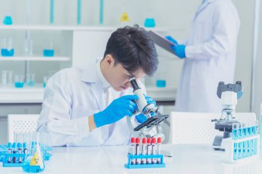 Erkek bilim adamı bilim laboratuarındaki mikroskop araştırmalarına bakar. Asyalı bilim adamı laboratuvar kimya laboratuvarlarını arıyor. Covid-19 Coronavirus biyokimya araştırma deneyi aşı konsepti