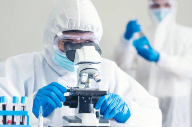 Erkek bilim adamı bilim laboratuarındaki mikroskop araştırmalarına bakar. Asyalı bilim adamı laboratuvar kimya laboratuvarlarını arıyor. Covid-19 Coronavirus biyokimya araştırma deneyi aşı konsepti