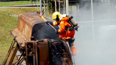 İtfaiyeci yangın hortumuyla, kimyasal köpüklü sprey motorla savaşıyor. İtfaiyeciler korunmak için kasketli, vücut korumalı üniformalı üniforma giyer. Yangın söndürücüde kurtarma eğitimi.