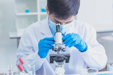Erkek bilim adamı bilim laboratuarındaki mikroskop araştırmalarına bakar. Asyalı bilim adamı laboratuvar kimya laboratuvarlarını arıyor. Covid-19 Coronavirus biyokimya araştırma deneyi aşı konsepti