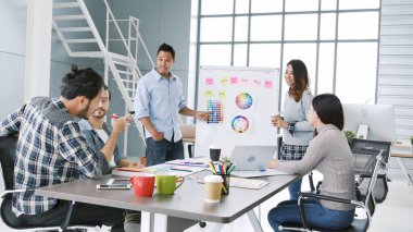 Çeşitli etnik gruplardan oluşan bir grup iş adamı konferans odasında toplantı yapıyor. İş grafiği, grafik ve veri bilgileriyle beyin fırtınası yapıyorlar. Takım çalışması iş birliği yapar. Güven ortakları bir araya gelir.