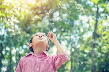 Yazın açık havada yeşil oyun sahasında sevimli, sevimli, neşeli köpüklü bir kız. Parktaki neşeli kız mutlu zamanlardı. Doğa parkında sabun üfleyen kabarcıklar..