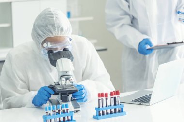 Erkek bilim adamı bilim laboratuarındaki mikroskop araştırmalarına bakar. Asyalı bilim adamı laboratuvar kimya laboratuvarlarını arıyor. Covid-19 Coronavirus biyokimya araştırma deneyi aşı konsepti