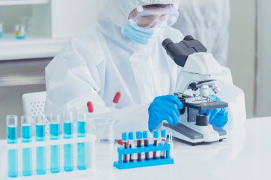 Erkek bilim adamı bilim laboratuarındaki mikroskop araştırmalarına bakar. Asyalı bilim adamı laboratuvar kimya laboratuvarlarını arıyor. Covid-19 Coronavirus biyokimya araştırma deneyi aşı konsepti