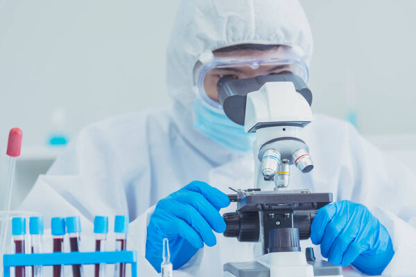 Male Scientist look into Microscope research in science laboratory. Asian scientist looking equipment laboratory chemistry labs. Covid-19 coronavirus biochemistry research experiment vaccine concept