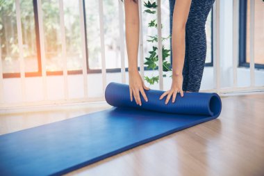 Kadın elleri yoga antrenman odasında jimnastik zemininde yoga minderini sardı. Egzersiz yapan kadın, köpüklü yoga paspası saran elleri kapıyor. Kadın yalınayak evde spor yapıyor sağlıklı yaşam tarzı konsepti