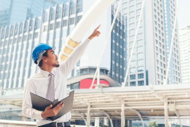 İnşaat mühendisi elleri inşaat mühendisliği için beyaz kaskı tutuyor. İnşaat mühendisi takım elbiseli adam inşaat sahasında beyaz kasklı kaskı elinde tutuyor.