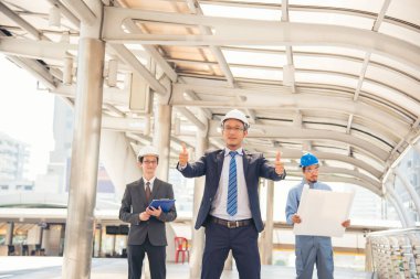 İnşaat mühendisi takımları modern kentteki inşaat sahasında birlikte çalışan işçi kaskı takıyorlar. Foreman Endüstri Mühendislik Mühendisliği ekip çalışması. Asya endüstrisi profesyonel takımı