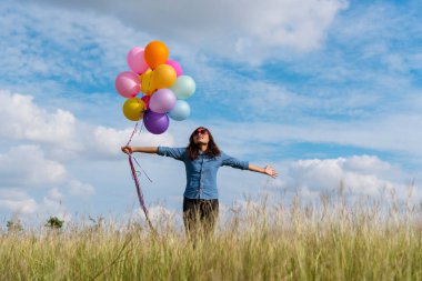 Yeşil çayır bulutu üzerinde koşan balonları tutan bir kadın. Mavi gökyüzü. Mutluluk dolu ve rahatlatıcı. Hava balonları tutan eller doğum günü partisinde oynar Mutlu zamanlar yaz güneşi açık havada