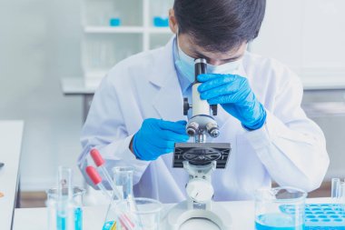 Erkek bilim adamı bilim laboratuarındaki mikroskop araştırmalarına bakar. Asyalı bilim adamı laboratuvar kimya laboratuvarlarını arıyor. Covid-19 Coronavirus biyokimya araştırma deneyi aşı konsepti