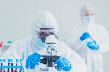 Erkek bilim adamı bilim laboratuarındaki mikroskop araştırmalarına bakar. Asyalı bilim adamı laboratuvar kimya laboratuvarlarını arıyor. Covid-19 Coronavirus biyokimya araştırma deneyi aşı konsepti