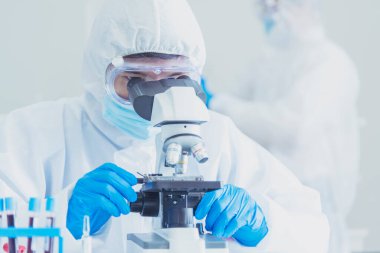 Erkek bilim adamı bilim laboratuarındaki mikroskop araştırmalarına bakar. Asyalı bilim adamı laboratuvar kimya laboratuvarlarını arıyor. Covid-19 Coronavirus biyokimya araştırma deneyi aşı konsepti