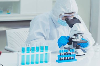 Erkek bilim adamı bilim laboratuarındaki mikroskop araştırmalarına bakar. Asyalı bilim adamı laboratuvar kimya laboratuvarlarını arıyor. Covid-19 Coronavirus biyokimya araştırma deneyi aşı konsepti
