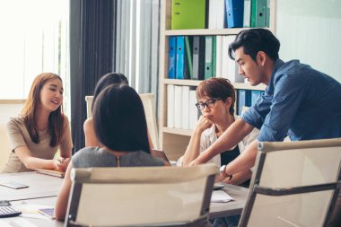 Mutluluk çeşitliliği iş dünyası ekibi şirket bürosu masasıyla toplantı odasında buluşuyor. Asyalı grup ortağı, toplantı odasında oturup fikir alışverişinde bulunan çok ırklı insanların beyin fırtınası yapıyor.