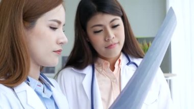 Asyalı tıp laboratuarındaki genç kadınlar birlikte sağlık hizmetleri yardım ekibini tartışıyorlar. İki Asyalı kadın doktor, dizüstü bilgisayarlı hasta danışmanlığı kullanarak doktorun muayenehanesiyle görüşmeyi tartışıyor.