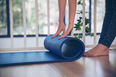 Kadın elleri yoga antrenman odasında jimnastik zemininde yoga minderini sardı. Egzersiz yapan kadın, köpüklü yoga paspası saran elleri kapıyor. Kadın yalınayak evde spor yapıyor sağlıklı yaşam tarzı konsepti