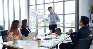 Bir grup iş adamı konferans odasında toplanıyor. Asyalı iş adamı konuşması, mevcut takım çalışması ortaklığı. Mutlu iş adamları toplantı odasında grafik çizelgesi yatırımı ve iş verilerini karşılıyorlar.