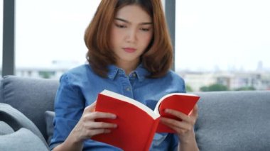 Oturma odasında kitap okuyan Asyalı kadın kitap okuyacak. Genç kadın gevşeme okuyucusu açık kitap boş zihin okuyor. Mutluluk, güzel kadın, gülen surat, mutlu zaman.