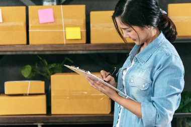 Stok malları teslimat paketlerini kontrol eden bir kadın. Asyalı bir kadın ev ofisinde küçük bir iş kuruyor. Çevrimiçi girişimci Asyalı kadın çevrimiçi kontrol tableti kullanıyor