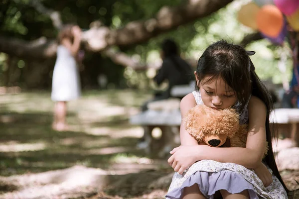 Sad girl hugging teddy bear sadness alone in green garden park. Lonely girl feeling sad unhappy sitting outdoors with best friend toy. Autism child play teddy bear best friend. Family violence concept