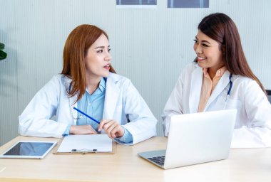 İki Asyalı kadın doktor dizüstü bilgisayarlı hasta danışmanlığı kullanarak doktorun muayenehanesiyle görüşmeyi tartışıyor. Asya tıp laboratuarındaki genç kadınlar birlikte sağlık hizmetleri ekip çalışmasını tartışıyorlar.