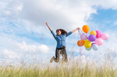 Yeşil çayır bulutu üzerinde koşan balonları tutan bir kadın. Mavi gökyüzü. Mutluluk dolu ve rahatlatıcı. Hava balonları tutan eller doğum günü partisinde oynar Mutlu zamanlar yaz güneşi açık havada