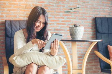 İnternetten dijital tablet alışverişi yapan Asyalı bir kadın arıyor, mesaj yolluyor, internet teknolojisi yaşam tarzında gülümsüyor. Asyalı kadın akıllı tablete dokunuyor mobil uygulama ev ofisini kullanarak ellere odaklanıyor.