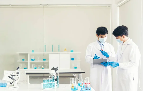 Two asian scientist team reserch chemistry science tube experiment biotech antibody sample in laboratory Cultivate Vaccine against covid-19 virus. Scientist consult, analyze in Chemistry Laboratory