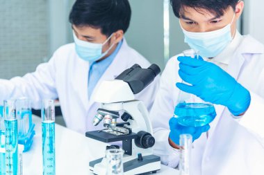 Bilim adamı bilim laboratuarındaki mikroskop araştırmalarını inceliyor. Asyalı bilim adamı laboratuvar kimya laboratuvarlarını arıyor. Covid-19 Coronavirus biyokimya araştırma deneyi aşı konsepti