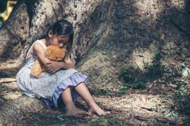 Üzgün kız, oyuncak ayıya sarılıyor. Üzüntü ağacının altında tek başına yeşil parkta oturuyor. Yalnız ve mutsuz bir kız dışarıda oturup en iyi arkadaşa sarılıyor. Otizmli çocuk oyuncak ayı en iyi arkadaşını oynuyor. Aile içi şiddet