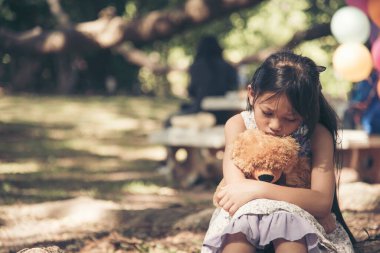 Üzgün kız, yeşil bahçe parkında yalnız başına oyuncak ayıya sarılıyor. En iyi arkadaş oyuncağıyla dışarıda oturan yalnız ve mutsuz bir kız. Otizmli çocuk oyuncak ayı en iyi arkadaşını oynuyor. Aile içi şiddet kavramı