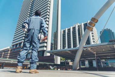 Mühendis elleri inşaat mühendisliği için beyaz kaskı tutuyor. Güvenlik giysisi giymiş inşaat mühendisi elleri şehir mühendisliği alanında beyaz işçi miğferini tutuyor.