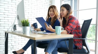 Asyalı iş arkadaşı arkadaşlığı, gülen yüzle. Mutluluk iki kadın meslektaşın ofis masasında takım çalışması. Bilgisayar şirketi ile çalışan takım ortakları