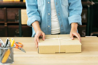 Kadın paket kutusunu masaya koydu. Müşteriye mal teslimatını kontrol ediyor. Asyalı bir kadın ofis masasında küçük bir iş kuruyor. Girişimci Asyalı kadın teslimat için ürün topluyor
