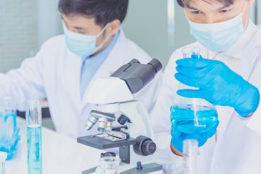 Bilim adamı bilim laboratuarındaki mikroskop araştırmalarını inceliyor. Asyalı bilim adamı laboratuvar kimya laboratuvarlarını arıyor. Covid-19 Coronavirus biyokimya araştırma deneyi aşı konsepti