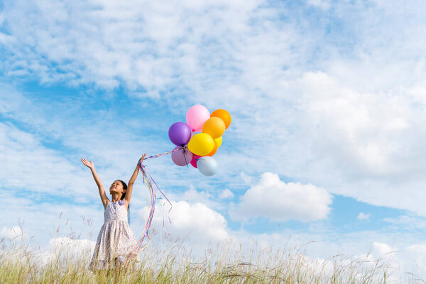 Cheerful cute girl holding balloons running on green meadow white cloud and blue sky with happiness. Hands holding vibrant air balloons play on birthday party happy times summer on sunlight outdoor