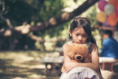 Üzgün kız, yeşil bahçe parkında yalnız başına oyuncak ayıya sarılıyor. En iyi arkadaş oyuncağıyla dışarıda oturan yalnız ve mutsuz bir kız. Otizmli çocuk oyuncak ayı en iyi arkadaşını oynuyor. Aile içi şiddet kavramı