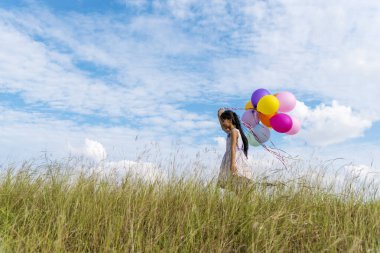Yeşil çayır üzerinde koşan balonlar tutan neşeli şirin kız beyaz bulut ve mutlulukla mavi gökyüzü. Hava balonları tutan eller doğum günü partisinde oynar. Mutlu zamanlar yaz mevsimi açık havada.