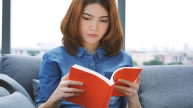 Oturma odasında kitap okuyan Asyalı kadın kitap okuyacak. Genç kadın gevşeme okuyucusu açık kitap boş zihin okuyor. Mutluluk, güzel kadın, gülen surat, mutlu zaman.