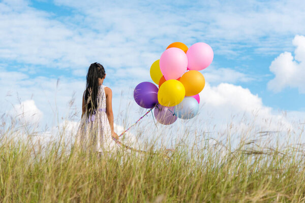 Cheerful cute girl holding balloons running on green meadow white cloud and blue sky with happiness. Hands holding vibrant air balloons play on birthday party happy times summer on sunlight outdoor