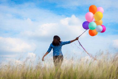 Yeşil çayır bulutu üzerinde koşan balonları tutan bir kadın. Mavi gökyüzü. Mutluluk dolu ve rahatlatıcı. Hava balonları tutan eller doğum günü partisinde oynar Mutlu zamanlar yaz güneşi açık havada